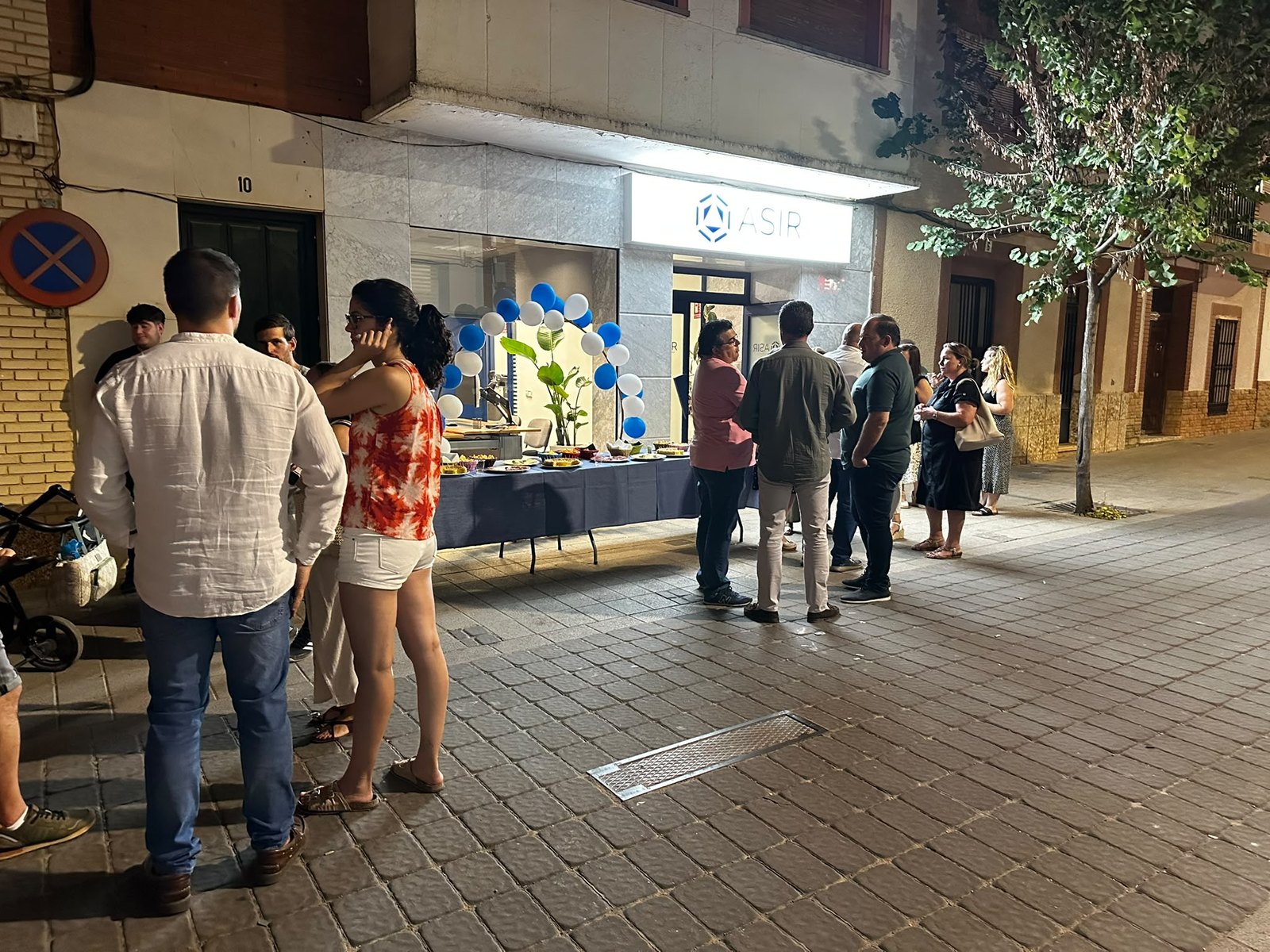 Asistentes a la inauguración de ASIR Ingeniería Informática frente al local, con un arco de globos azul y blanco